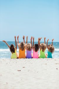 A joyful group of women with hands raised enjoying a sunny day at Santa Monica Beach.